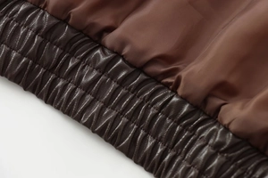 Macro detail of dark brown faux leather bomber jacket with elastic hem and inner lining