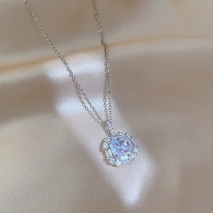 Macro shot of silver square pendant necklace with emerald-cut zirconia on silk fabric