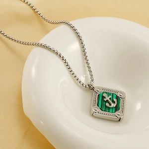 Retro stainless steel anchor pendant necklace with green striped inlay on a white bowl