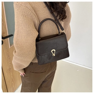 Detail of a dark brown vintage crossbody bag with a golden horseshoe buckle on the flap