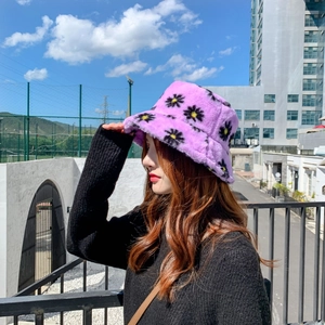 Purple plush bucket hat with daisy patterns shown on a model in outdoor setting