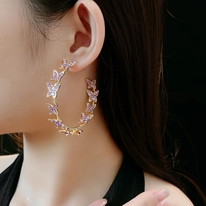 Détail de créoles dorées en C avec papillons en cristal violet sur mannequin