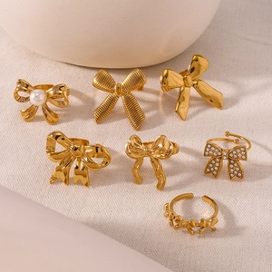 Set of seven golden bowknot rings with pearls and zircons on a textured fabric background