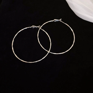 Close-up of silver geometric hoop earrings with textured finish on black velvet backdrop