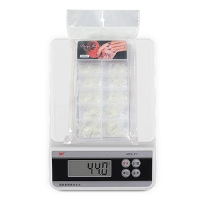 Detailed view of 100pcs clear false nail tips in a 10-slot storage box on a scale