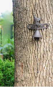 Detail of vintage cast iron welcome bell with bird statue and hanging rope on a tree