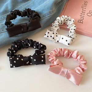 Close-up of four satin bow scrunchies in solid colors and polka dot patterns on books