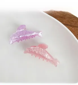Detail view of shimmering glitter dolphin hair clips in lilac and pink on white plate
