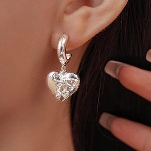 Close-up of silver heart drop earrings with bow detail and sparkling zircon crystals