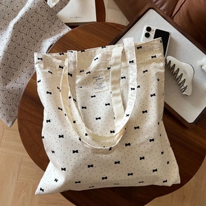 Detailed top view of a cream canvas tote with black bow patterns on a rustic wooden table
