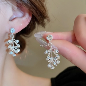 Close-up of sparkling leaf-shaped drop earrings with clear zircons on a model