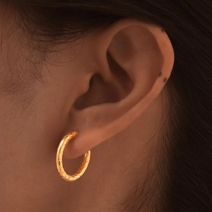Close-up of golden hoop earring with quilted diamond texture on an earlobe
