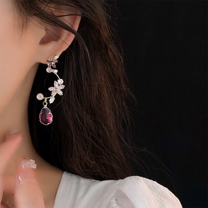Elegant gold flower drop earrings with purple crystals worn by a model on black background