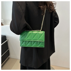 Detailed view of green quilted leather chain strap crossbody bag worn with black suit
