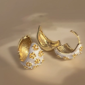 Detailed close-up of golden C-shaped hoop earrings with white enamel floral patterns
