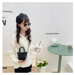 Toddler girl modeling a black mini bow crossbody bag with a white knit sweater