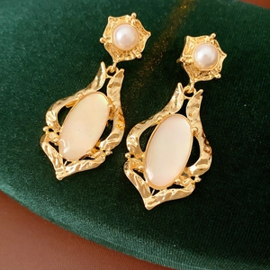 Détail de boucles d'oreilles vintage dorées avec nacre ovale et fleur de perle sur velours