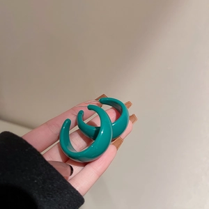 Close-up of vibrant teal green acrylic C-shape hoop earrings with silver pins