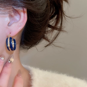 Close-up of vintage C-shaped gold hoop earrings with dark blue enamel on a female model