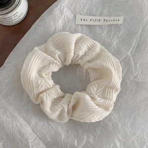 Detailed close-up of cream textured knitted hair scrunchie on elegant white tissue paper