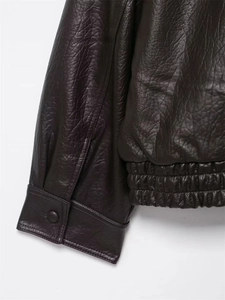 Detail of dark brown faux leather jacket showing buttoned cuffs and elasticated hemline