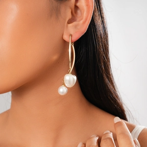 Boucles d'oreilles longues dorées avec deux perles blanches portées par un mannequin