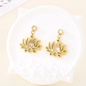 Détail de boucles d'oreilles lotus dorées avec zircons en goutte sur un plateau blanc