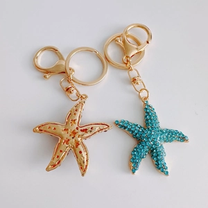 Close-up of gold metal and turquoise crystal starfish keychains on white background