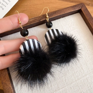 Close-up of retro black and white striped pom-pom earrings on a fabric wooden tray