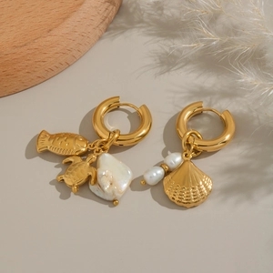 Detail view of gold fish shell and baroque pearl asymmetric earrings on a wooden tray