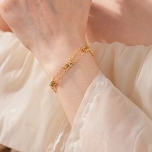 Detailed view of vintage gold layered bracelet with ornate square flower charms on wrist