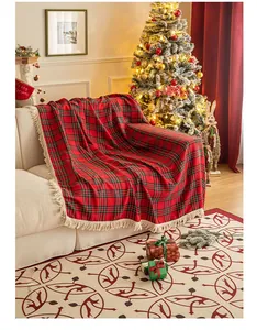 Detail of red plaid Christmas throw blanket with white tassels on a cozy white sofa