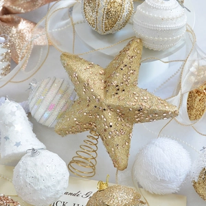 Flat lay of champagne gold star tree topper with glitter ornaments and velvet pearls