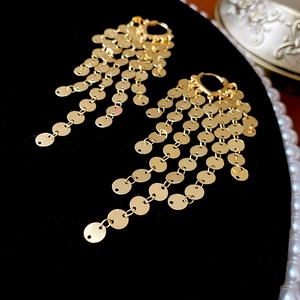 Macro shot of gold sequin tassel earrings with mirror finish on black velvet background