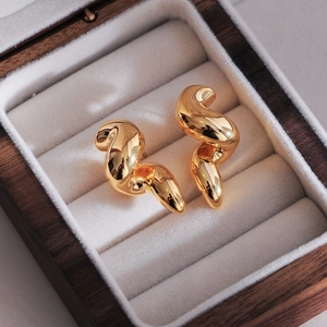 Close-up of golden spiral teardrop earrings on a white velvet jewelry box tray