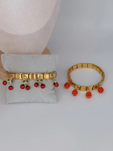 Macro view of gold modular charm bracelet featuring detailed strawberry and cherry pendants