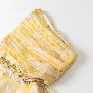 Detail of yellow floral chiffon dress featuring pleated fabric and criss-cross tie design