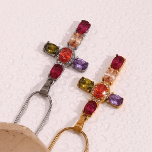 Macro shot of 18K gold and silver cross pendants with colorful zircons on wet background