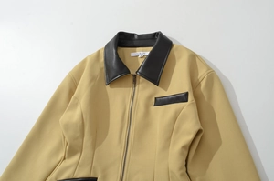 Flat lay detail of women's khaki jacket with black leather patchwork and metal zipper