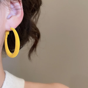 Détail d'une femme portant une grande boucle d'oreille ronde jaune floquée à texture mate