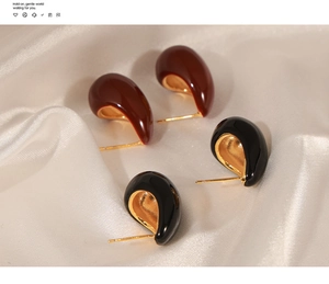 Detailed view of black and burgundy drop earrings with gold interior on white silk fabric