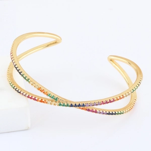 Detailed close-up of a gold X-shaped criss-cross open bangle with rainbow zircon stones