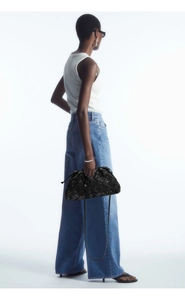 Fashionable black woven leather dumpling bag held by a model in a minimalist studio