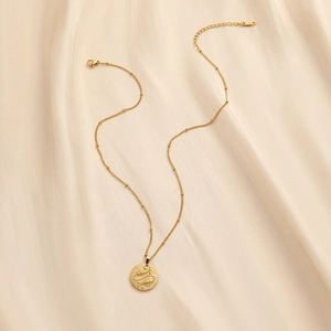 Detail of gold coin necklace with snake relief on a soft beige silk background