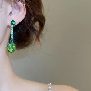 Close-up of elegant gold earrings with vertical green zircons and heart drop