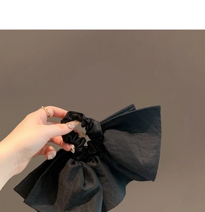 Detail of black oversized scrunchie featuring pleated glossy fabric and layered ruffles