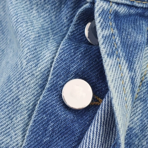 Macro detail of silver metal button and textured denim fabric on high waist jeans