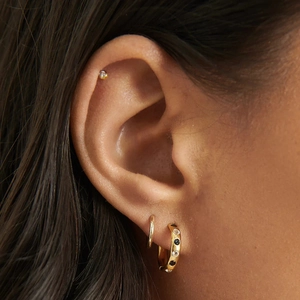 Detailed view of model wearing gold earrings with black and white zircon stone inlay