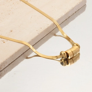 Detailed shot of golden snake bone chain necklace with three beads on stone surface