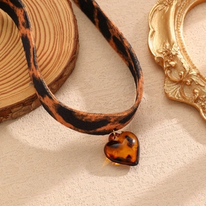 Dettaglio del choker leopardato con ciondolo a cuore ambrato su sfondo rustico